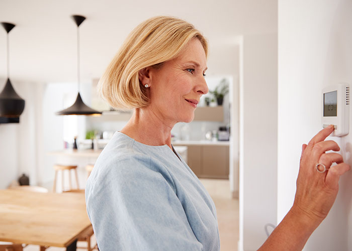 Mature Woman Adjusting Central Heating Temperature At Home On Thermostat